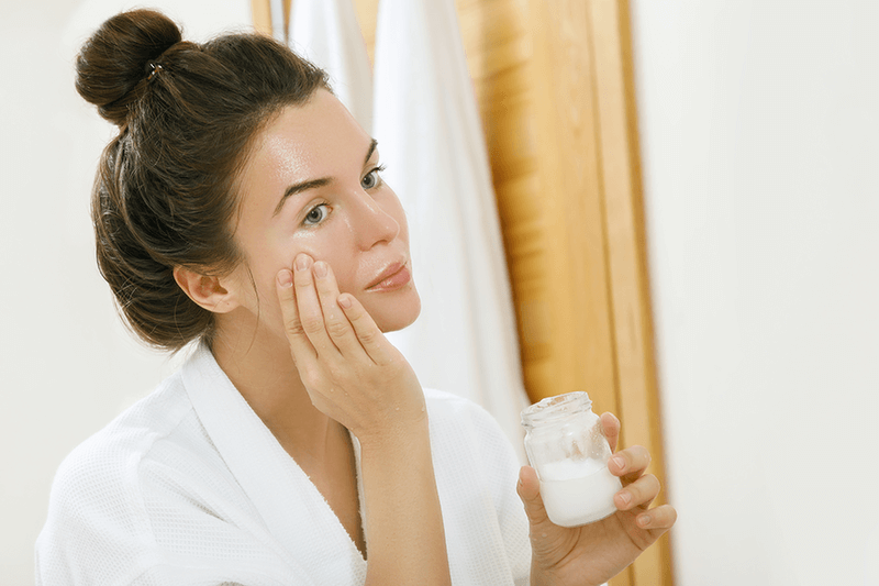 Woman applying coconut oil on her face.